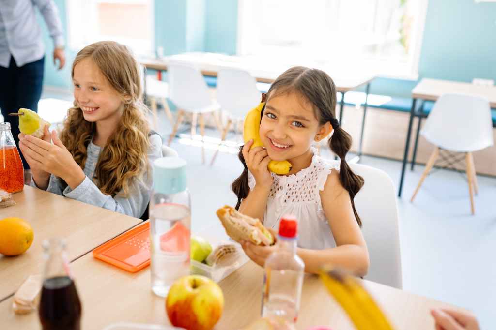 Zwei lachende Mädchen die Frühstückspause in der Schule haben. Links, blonde Haare und eine Birne in der Hand. Rechts, braune Haare und eine Banane wie ein Telefon am Ohr gehalten.
#zcatering #caterer #berlin #kitacaterer #schulcaterer #regional #qualitativ #gesund #biocaterer #Mittagessen #Ernährung #ausgewogeneErnährung #Berlinmitte #BerlinerFamilienunternehmen